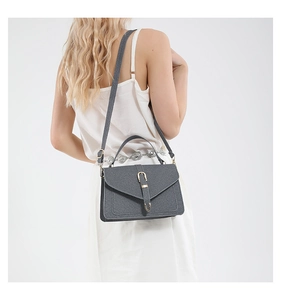 Model wearing dark grey textured crossbody bag with gold U-buckle on white background