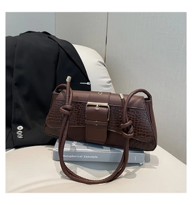 Detail of dark brown faux crocodile leather bag with golden buckle and knot strap design
