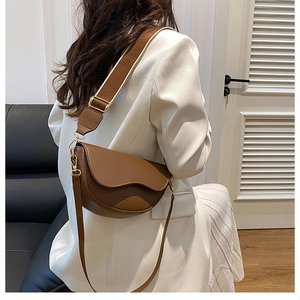 Détail d'un sac besace marron avec doubles bandoulières et boucle dorée sur modèle