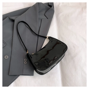 Detail of glossy black patent leather baguette bag with elegant gold metal buckle