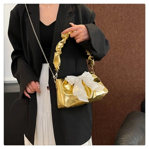Detail of gold metallic bag with pleated handle and white organza bow on model