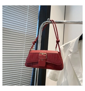 Detail of burgundy crocodile-embossed leather bag with large metal buckle and knotted strap