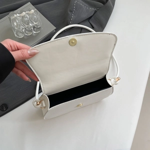 Overhead view of a white PU leather shoulder bag with gold magnetic clasp and black lining