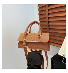 Close-up of brown textured crossbody bag featuring gold metal bar and woven fabric detail