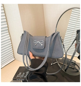 Gros plan sur un sac bandoulière en denim gris avec détail de nœud en métal argenté