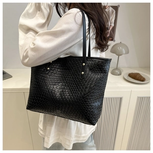 Close-up of black woven tote bag featuring gold stud accents and dual shoulder straps