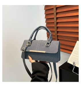 Detail of dark blue denim crossbody bag featuring a gold metal bar and twill texture