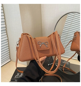 Détail d'un sac baguette orange tissé avec une boucle nœud en métal argenté poli