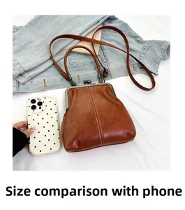 Brown vintage kiss-lock handbag size comparison with a smartphone on denim