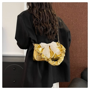 Detail of gold metallic pleated handbag with a large white organza bow on a black suit