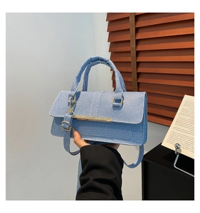 Detail of light blue denim crossbody bag with gold metal trim and rectangle flap design