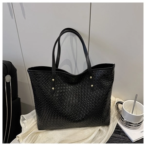 Detail of black woven tote bag featuring gold rivet accents and spacious textured design