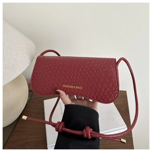 Detail of dark red crossbody bag with woven texture and gold lettering hand-held indoors