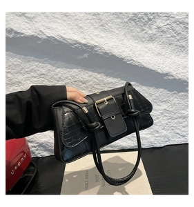 Detail of black crocodile texture bag with double knotted straps and large metal buckle