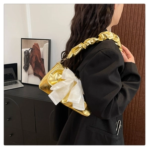 Detail of a shiny gold metallic shoulder bag featuring a large white bow and pleated strap