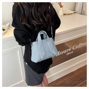 Light blue tote bag with stripe detail shown being worn by a model in a cafe setting