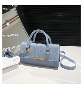 Detail showing light blue denim texture handbag with gold metal clasp on white table
