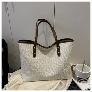 Detail of woven texture on cream tote bag with dark brown handles and gold rivets
