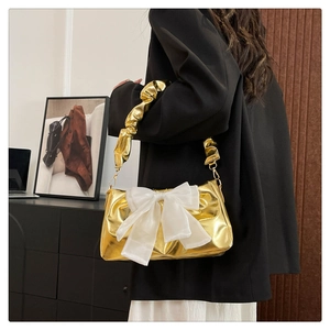 Detail of metallic gold shoulder bag featuring a large white bow and pleated handle