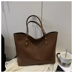 Macro view of woven textured dark brown tote bag with elegant gold rivet details
