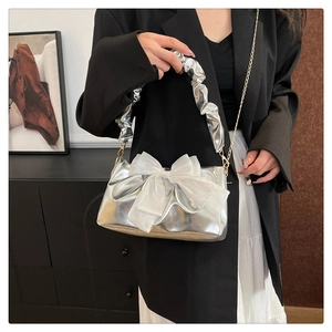 Detail of silver metallic handbag with oversized white organza bow and gold chain strap
