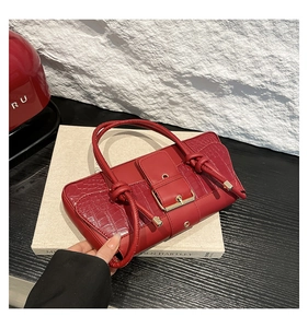 Detail of burgundy crocodile-embossed handbag with elegant gold buckle and knot handle