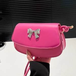 Rose pink saddle shoulder bag with silver bow detail held by a hand over a table