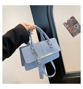 Detail of light blue twill denim handbag featuring a gold metal bar and wide shoulder strap