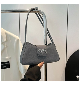 Detalle de bolso de hombro gris con textura vaquera y lazo metálico de plata