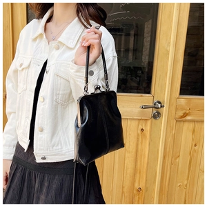 Retro black leather frame bag with metal clasp closure held by model in casual outfit