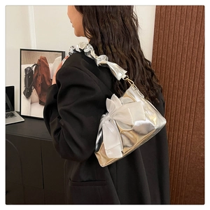 Detail of silver metallic underarm bag featuring a white bow and ruched shoulder strap