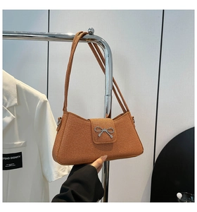 Detalle del bolso baguette marrón con textura y hebilla de lazo metálico plateado