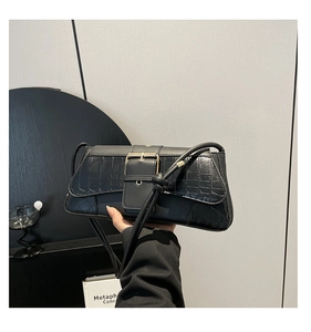 Close-up of black faux leather handbag featuring crocodile pattern and gold metal buckle