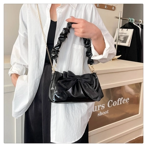 Detail of black glossy handbag with bow decoration, pleated handle and gold chain strap