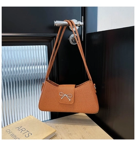 Détail du sac sous le bras texturé caramel avec nœud argenté sur une poignée de porte noire