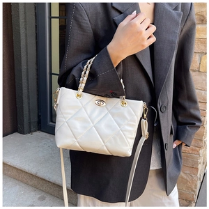 Detail of white quilted handbag with golden chain handle and oval twist lock closure
