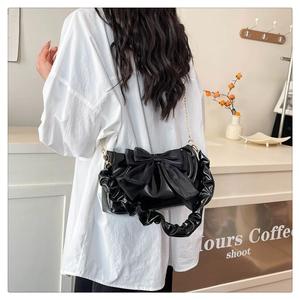 Detail of black glossy cloud bag with large bow and gold chain on a white shirt