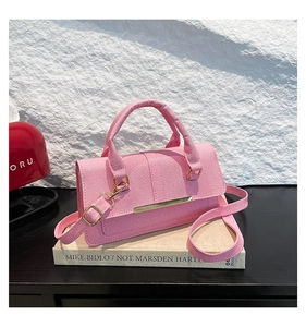 Close-up of pink fabric crossbody bag with gold hardware and removable strap on books