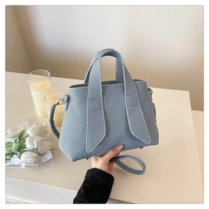 Close-up of light blue textured crossbody tote bag with dual straps and stylish striped pattern