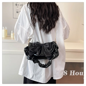 Detail of black glossy shoulder bag with a large bow and elegant chain strap on a model
