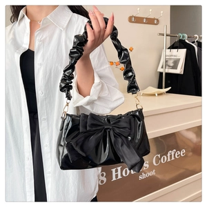 Close-up of black patent leather shoulder bag featuring a large satin bow and ruffled strap