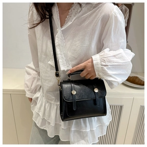 Detail of a vintage black leather crossbody bag with elegant gold round buckle accents