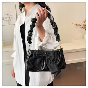 Close-up of black glossy shoulder bag featuring a large satin bow and ruffled strap detail