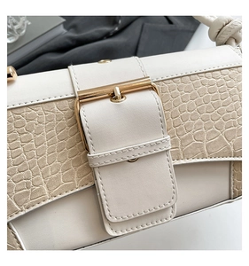 Detail of cream-colored shoulder bag featuring crocodile pattern leather and gold metal buckle
