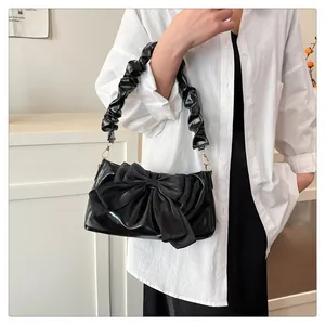 Detail of black patent leather shoulder bag with large bow and ruffled strap detail