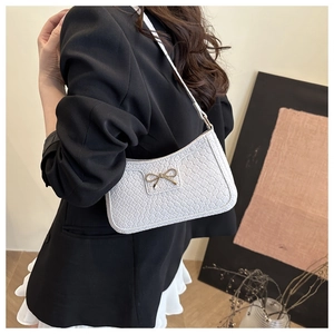 Détail du sac à bandoulière blanc à texture tressée et nœud doré sur veste