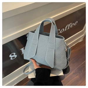 Detail of light blue striped tote bag featuring woven texture and chic top handle design