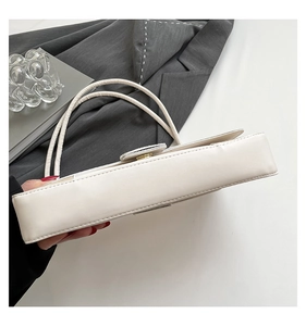 Close-up of a white faux leather shoulder bag with a metal buckle and fine grain texture