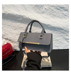 Close-up of grey denim texture handbag featuring golden metal bar and hardware detail