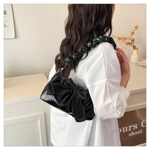 Detail of black glossy shoulder bag featuring a large bow and ruched scrunchie strap